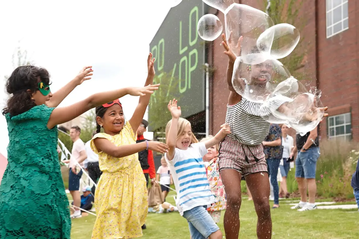 Children chasing giant bubbles on the green at a community event