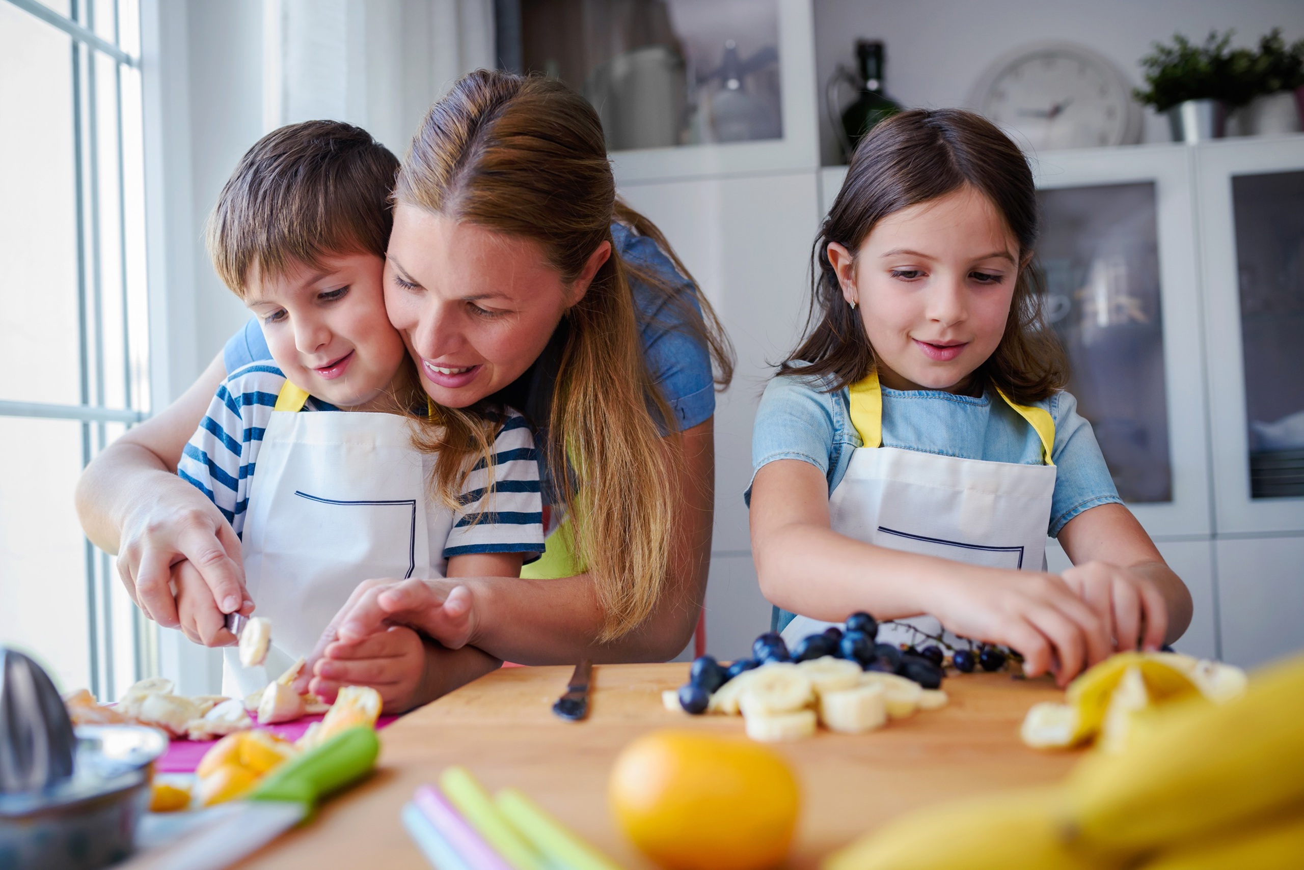 A mum and her two children cooking together in a bright kitchen