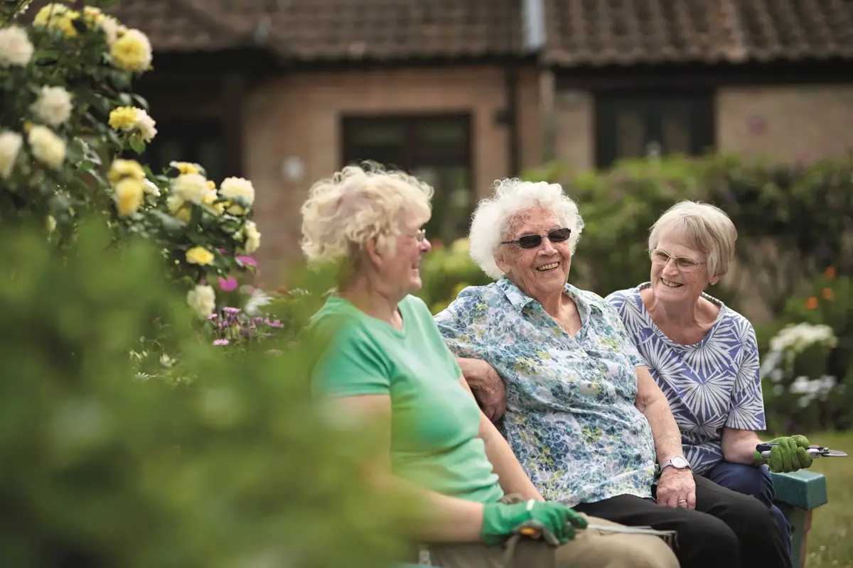 Three neighbours chatting on a bench in a shared garden